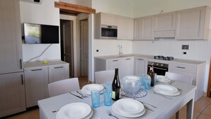 A modern kitchen with white cabinets, a built-in oven, and a dining area set for four with plates, glasses, and cutlery. - Lovely apartment for 6 people with WIFI, pool, A/C, TV and terrace (Budoni)