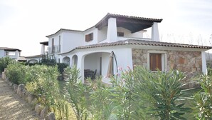 A two-story house with a white exterior, stone accents, and a tiled roof. - Lovely apartment for 6 people with WIFI, pool, A/C, TV and terrace (Budoni)