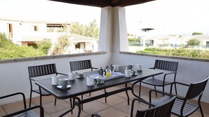 A covered outdoor patio with a table set for four, surrounded by chairs, overlooking a residential area with houses and greenery. - Lovely apartment for 6 people with WIFI, pool, A/C, TV and terrace (Budoni)