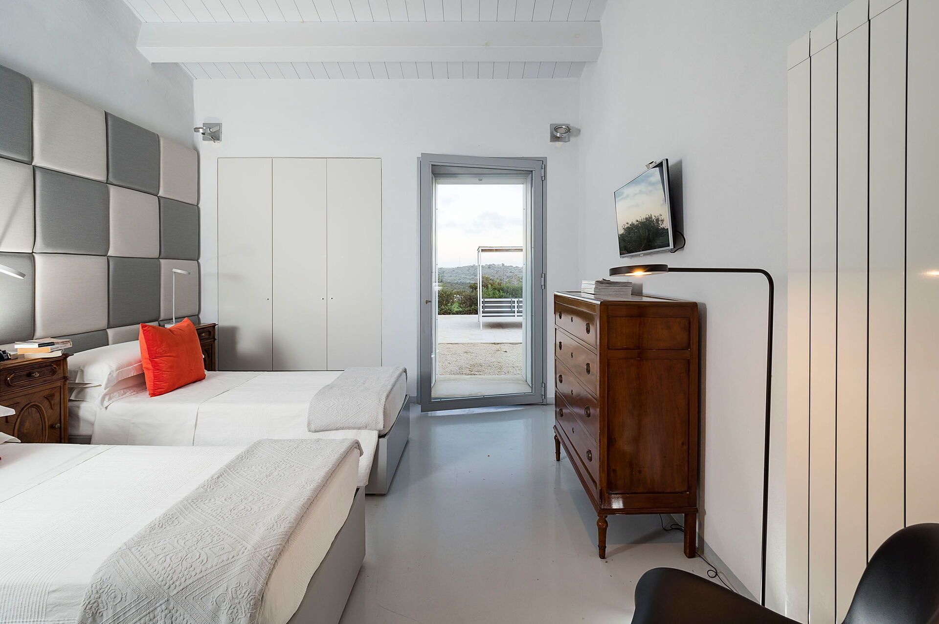 Une chambre moderne avec deux lits, une commode en bois, un téléviseur et une vue sur l’extérieur.