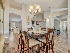 A spacious dining area with a large glass table and wooden chairs, a chandelier, and a view into the kitchen. - Mid-Sand Creek (Colorado Springs)