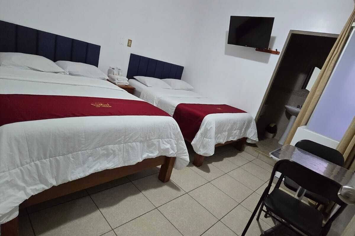 Une chambre d’hôtel avec deux lits, une petite table, une chaise et un téléviseur fixé au mur.