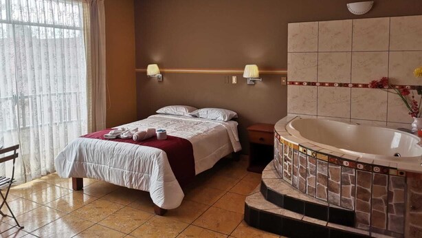 A hotel room with a bed, two bedside lamps, a bathroom with a bathtub, and a ceiling fan. - HOTEL LOS ANGELES (Huaral)