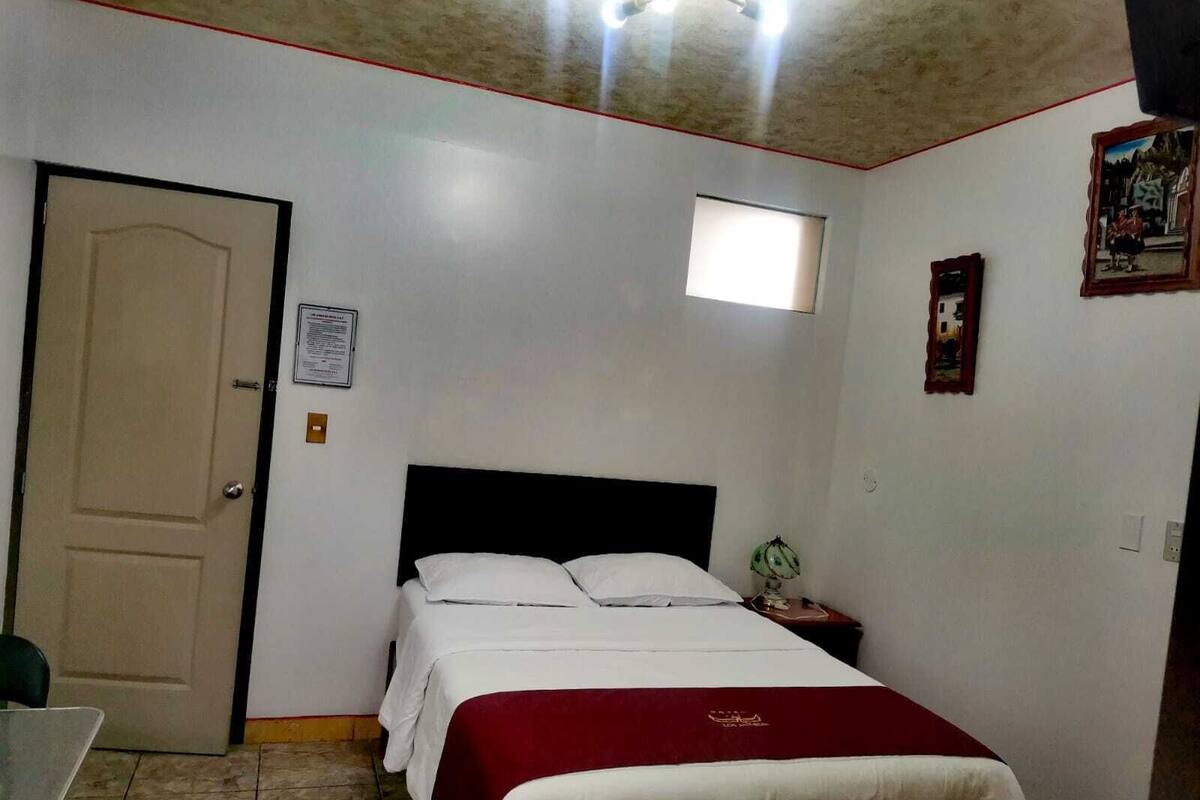 Une chambre à coucher avec un lit, une table de chevet, une chaise, une porte et une petite fenêtre.