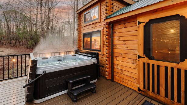 Een houten chalet met een hottub op een terras, omringd door bomen.