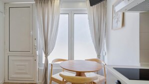 A compact room with a round wooden table and two chairs, a white door, and a window with curtains. - Felp Santa Maria 1 (Setúbal)