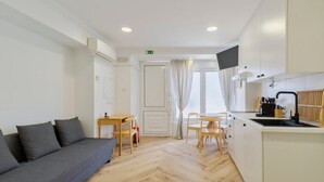 A modern, well-lit room with a sofa, a small dining table, and a kitchen area with a sink and cabinets. - Felp Santa Maria 1 (Setúbal)