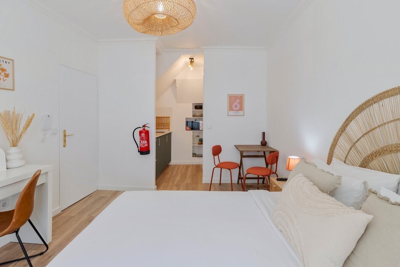 Ein Schlafzimmer mit einem Bett, einem Schreibtisch und einem Stuhl. An der Wand hängt ein Feuerlöscher und es steht ein kleiner Tisch mit Stühlen bereit.