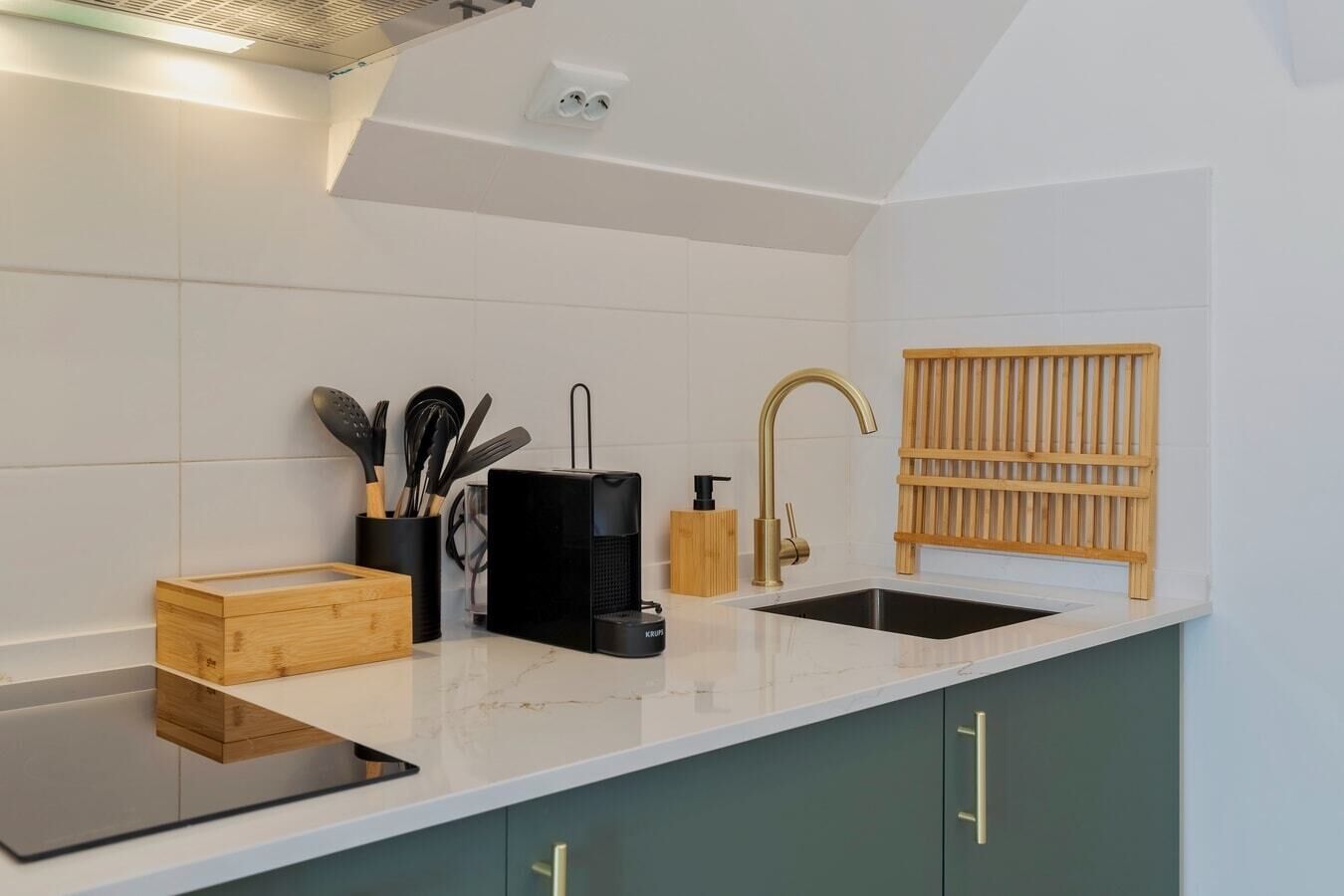 A kitchen with a white countertop, a black appliance, a wooden rack, and green cabinets.