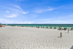 A wide sandy beach with green umbrellas and lounge chairs.