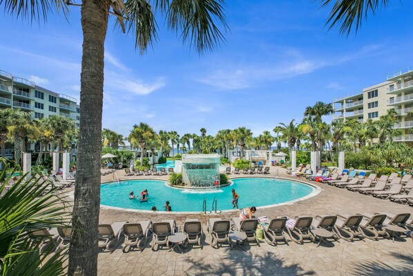 A resort pool area with lounge chairs, palm trees, and a central water feature.