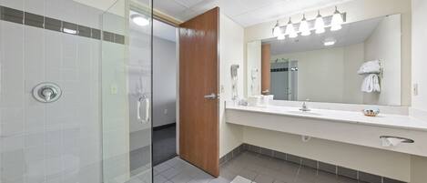 A modern bathroom with a glass shower enclosure, a wooden door, a large mirror, and a white sink with a towel rack.