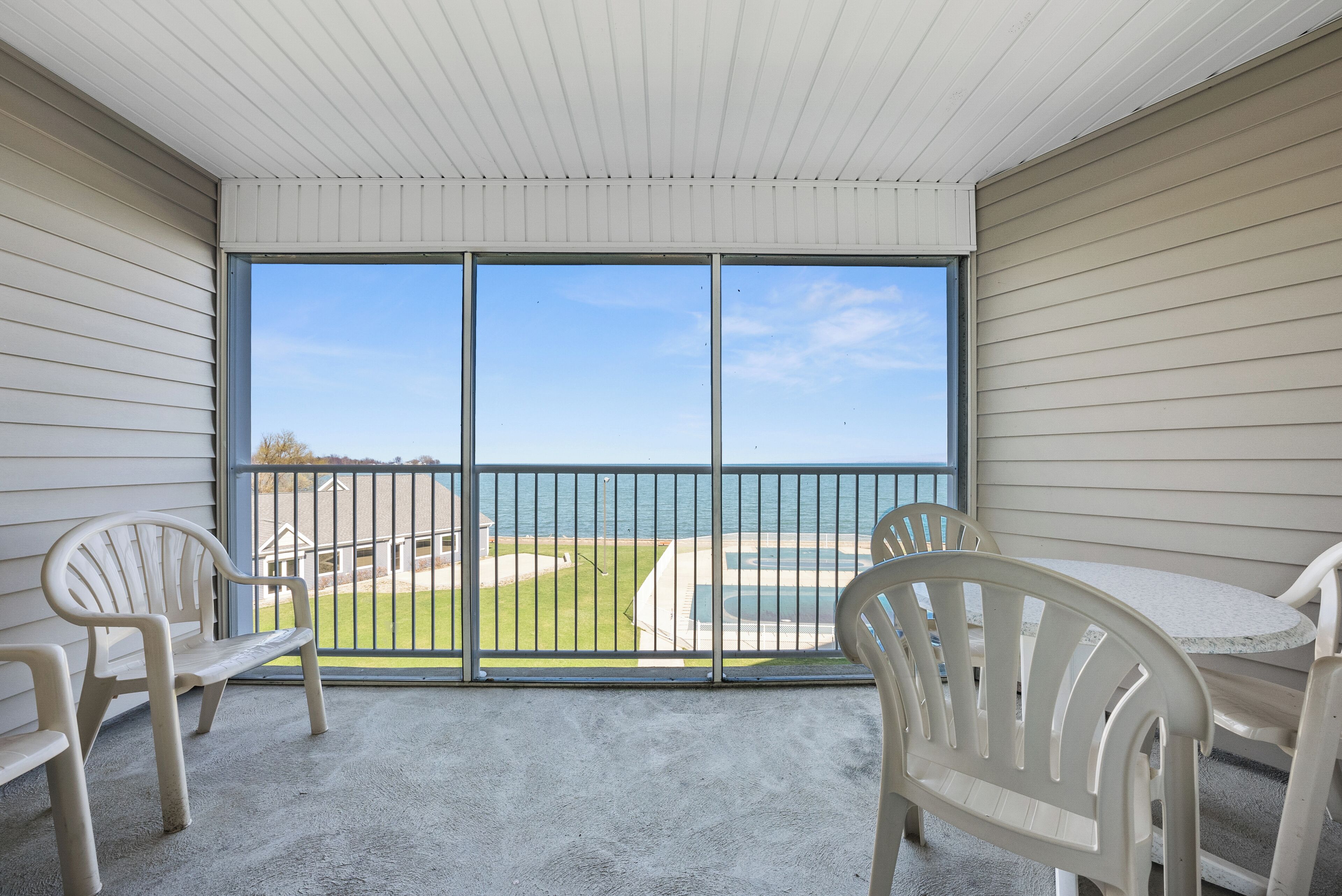 A balcony with a view of the ocean, a concrete floor, and two white plastic chairs.