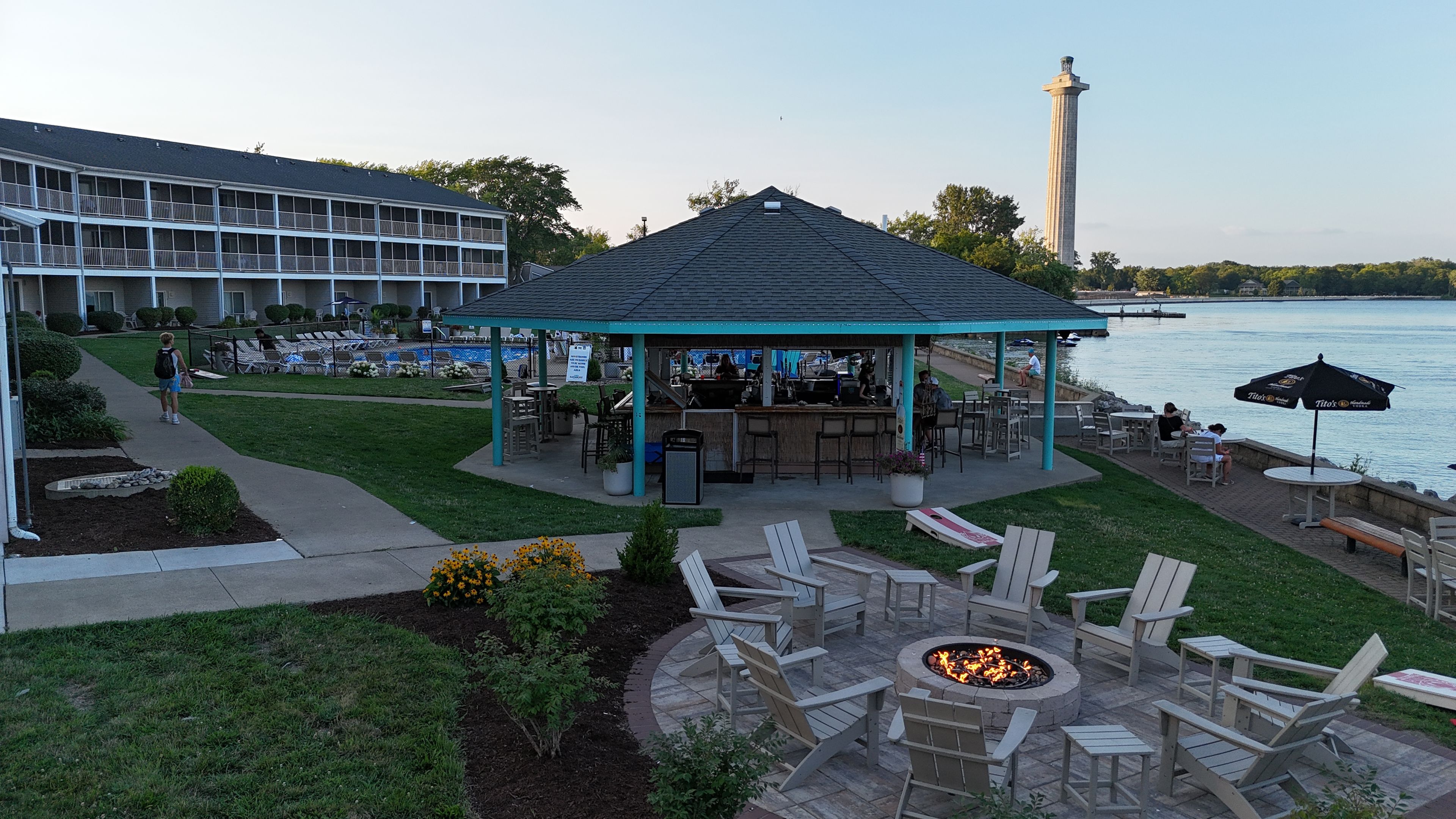 A gazebo with outdoor seating, a pool, and a view of a body of water with a tower in the distance.