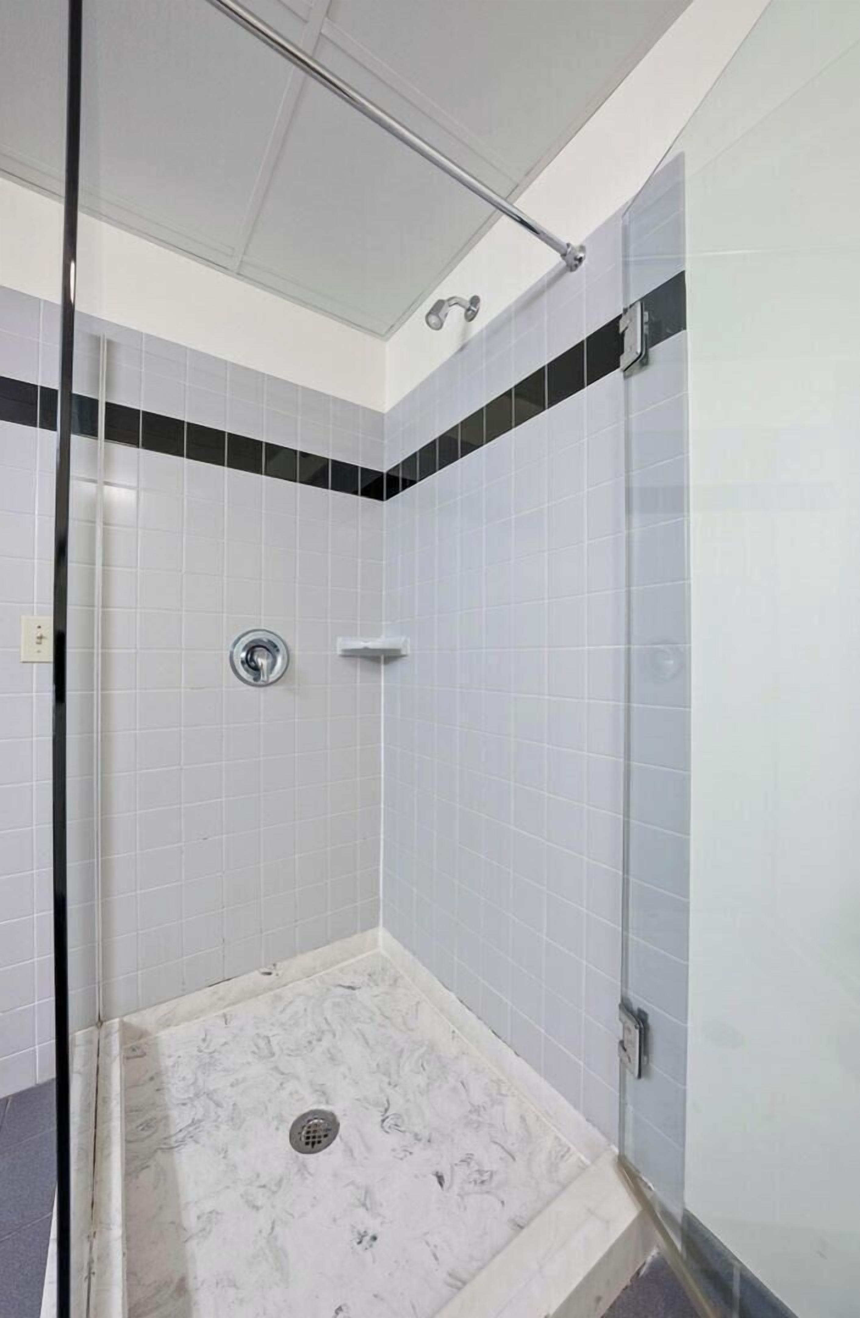 Ducha moderna con azulejos blancos y puerta de cristal, que incluye un panel de control y un cabezal de ducha.