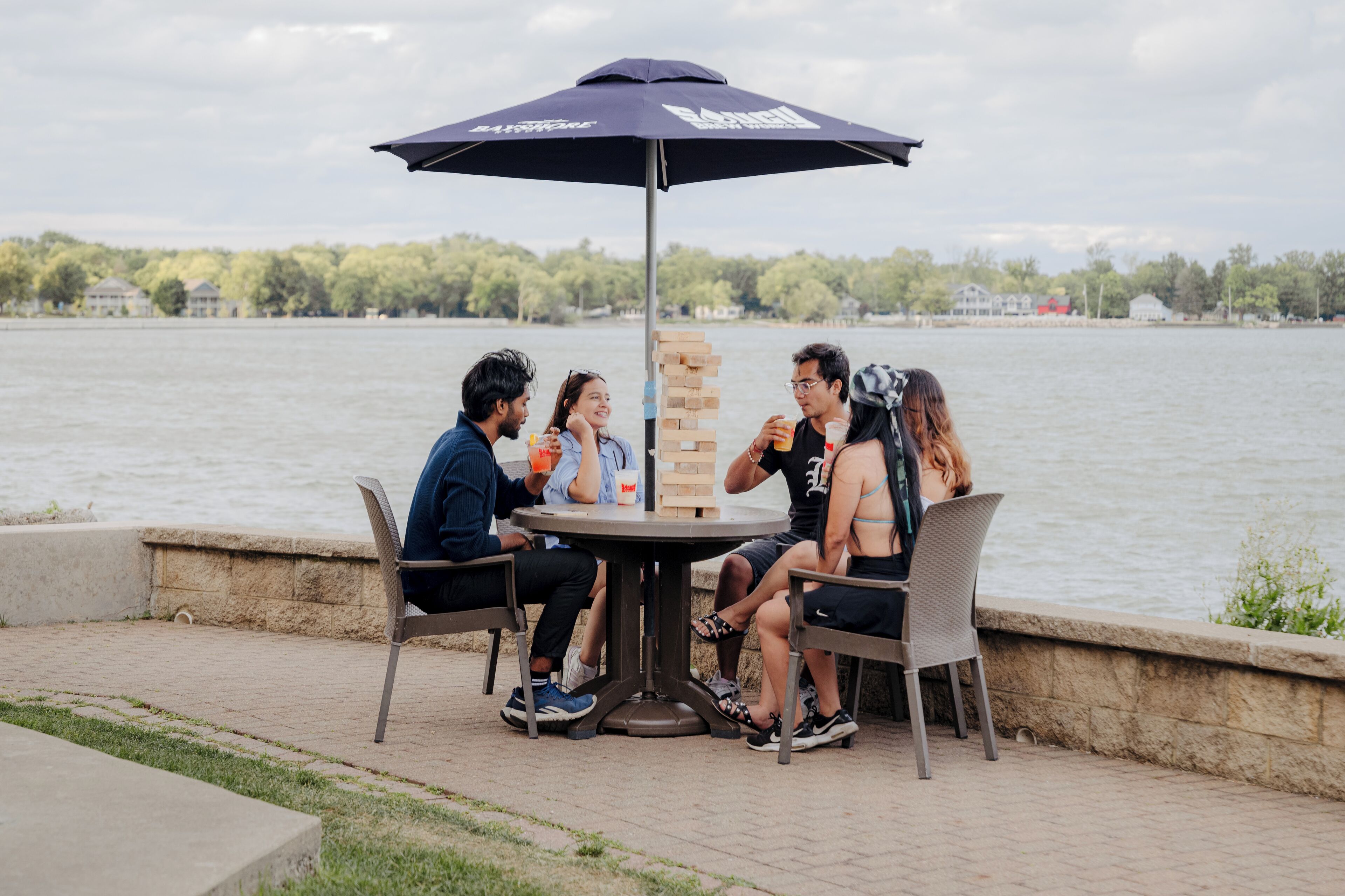 A group of people playing a board game at an outdoor table with a view of a lake.