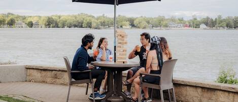 A group of people playing a board game at an outdoor table with a view of a lake.