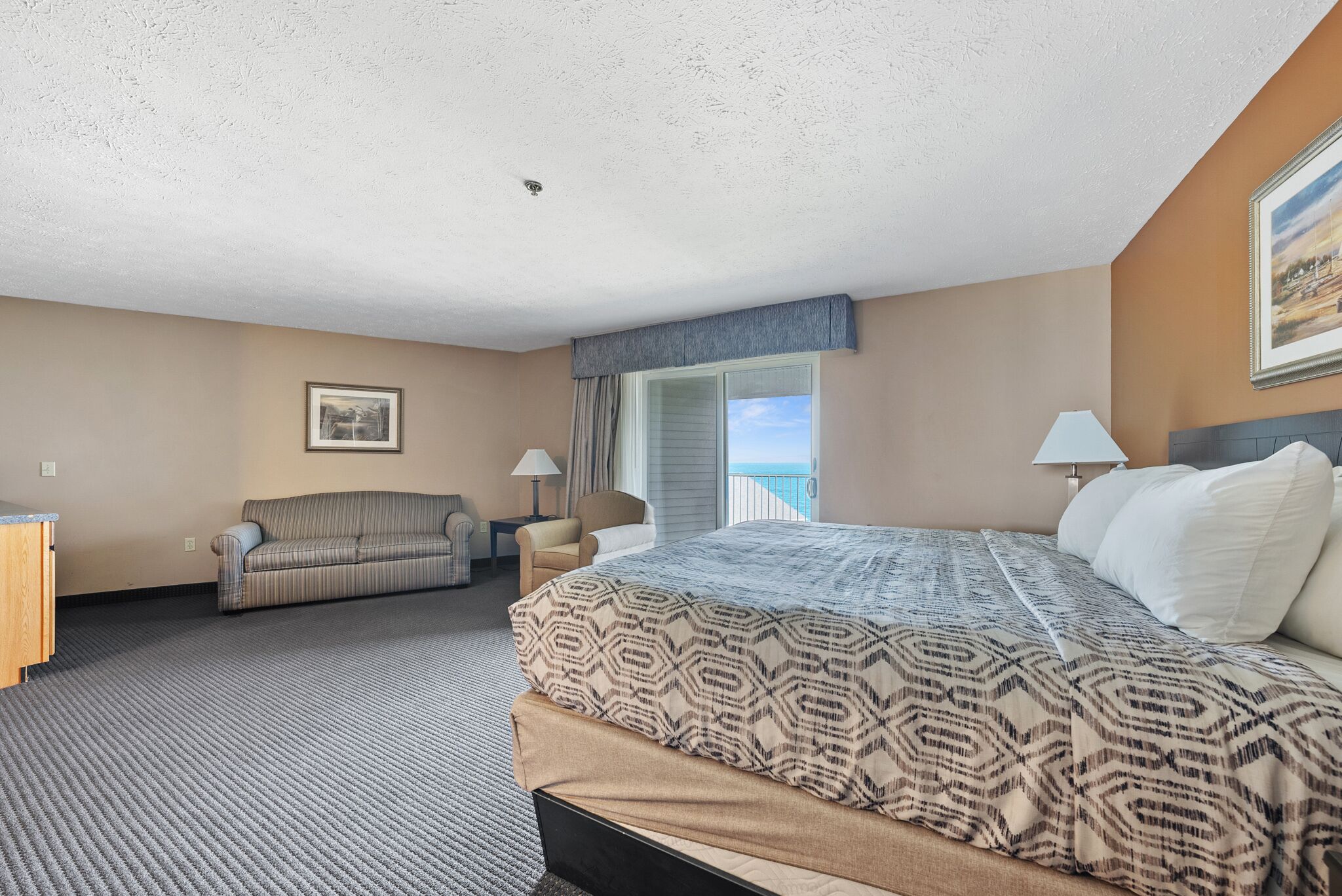 Quarto de hotel com uma cama grande, um sofá, uma cadeira, uma escrivaninha e uma janela com vista.