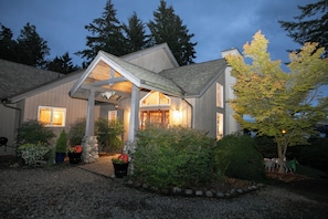 Une maison moderne dotée d’un porche abrité, entourée d’un jardin bien entretenu et d’arbres.