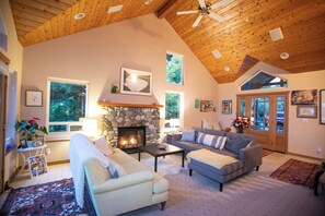 A cozy living room with a stone fireplace, two sofas, a coffee table, and a ceiling fan.