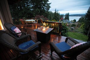 Una terraza de madera con mobiliario de mimbre y una mesa central con chimenea.