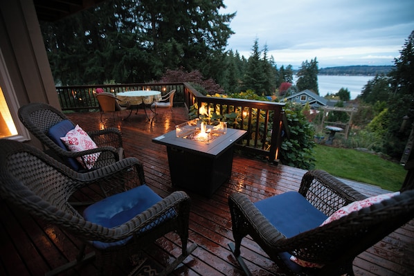 Une terrasse en bois, meublée de meubles en osier, avec une table centrale agrémentée d’un foyer.