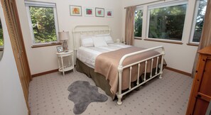 A bedroom with a bed, bedside table, lamp, framed pictures, and a window.