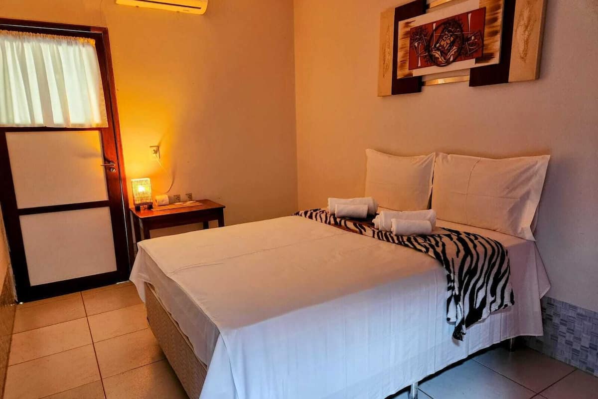 Quarto de hotel com cama, mesa de cabeceira, luminária e quadro na parede.