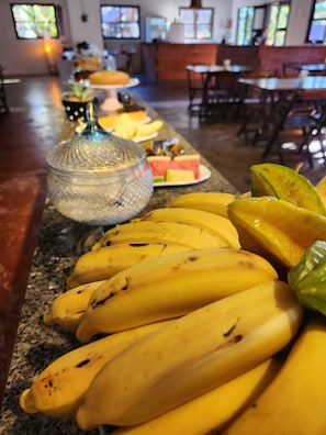 A buffet table with bananas, watermelon, and a glass container.