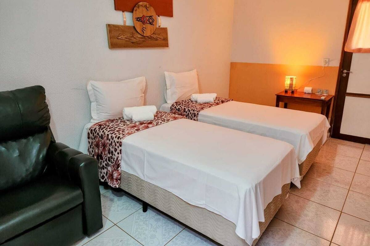 Quarto de hotel com duas camas, um sofá, um relógio na parede e uma mesa de cabeceira com abajur.