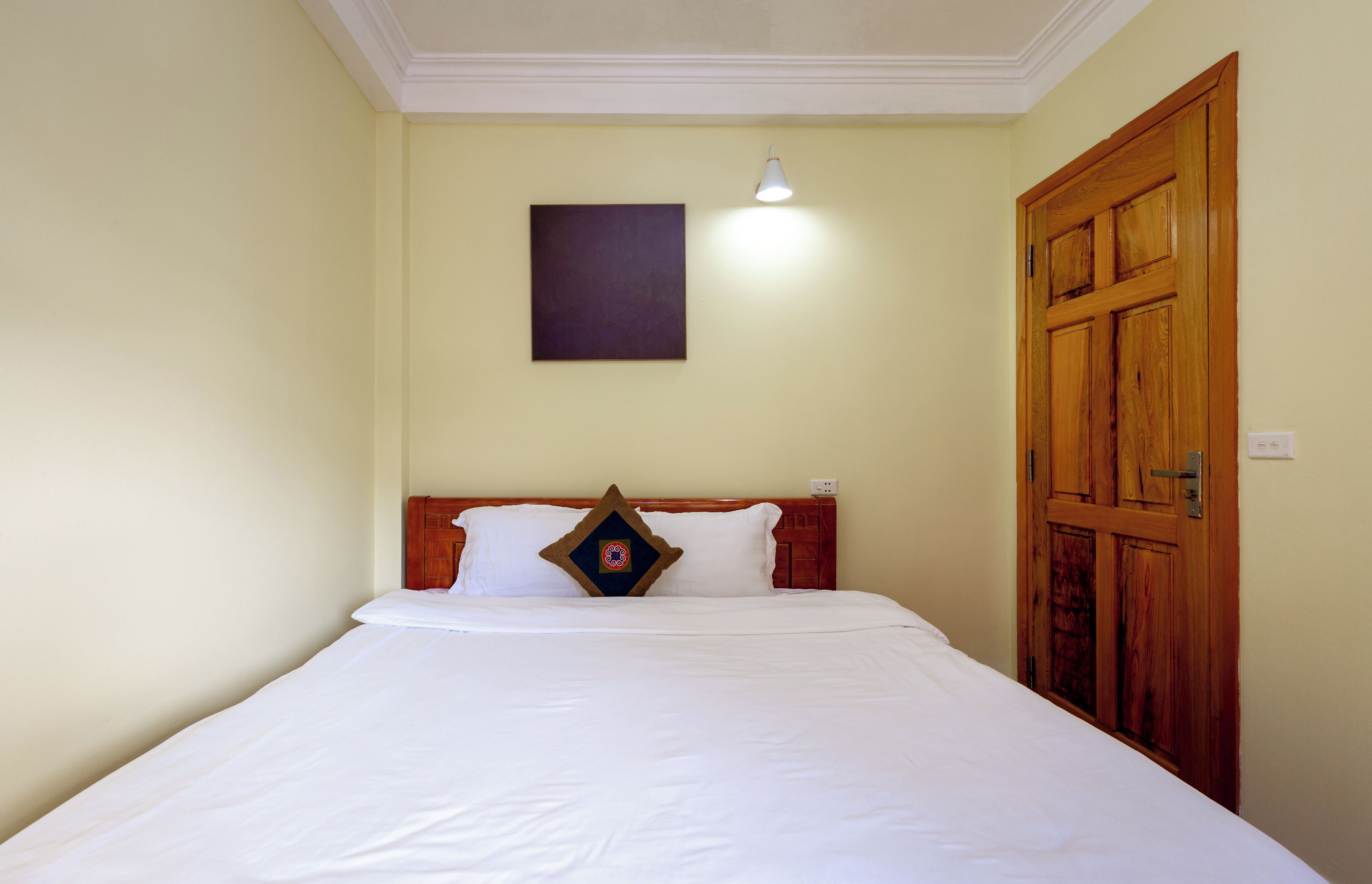 A neatly made bed with white linens, a wooden headboard, and a single decorative pillow.