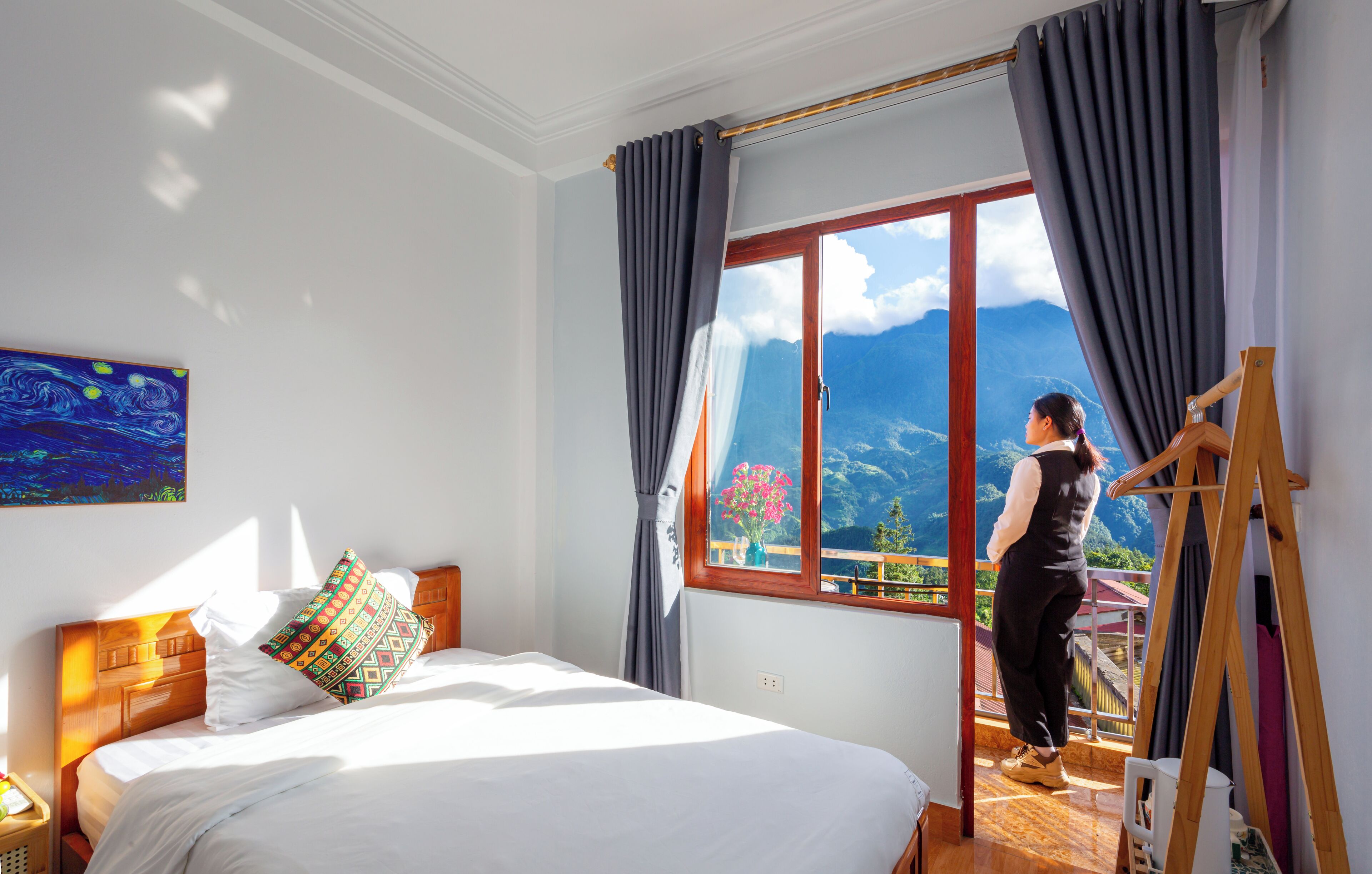 Habitación de hotel con una cama grande, cabecero de madera, un cuadro en la pared y una ventana con vistas a la montaña.