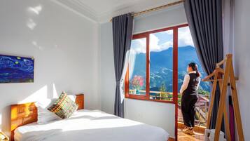Habitación de hotel con una cama grande, cabecero de madera, un cuadro en la pared y una ventana con vistas a la montaña.