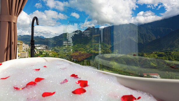 A bathtub with red rose petals, a window view of mountains, and a cityscape. - Moc Home Sapa Center (Sa Pa)