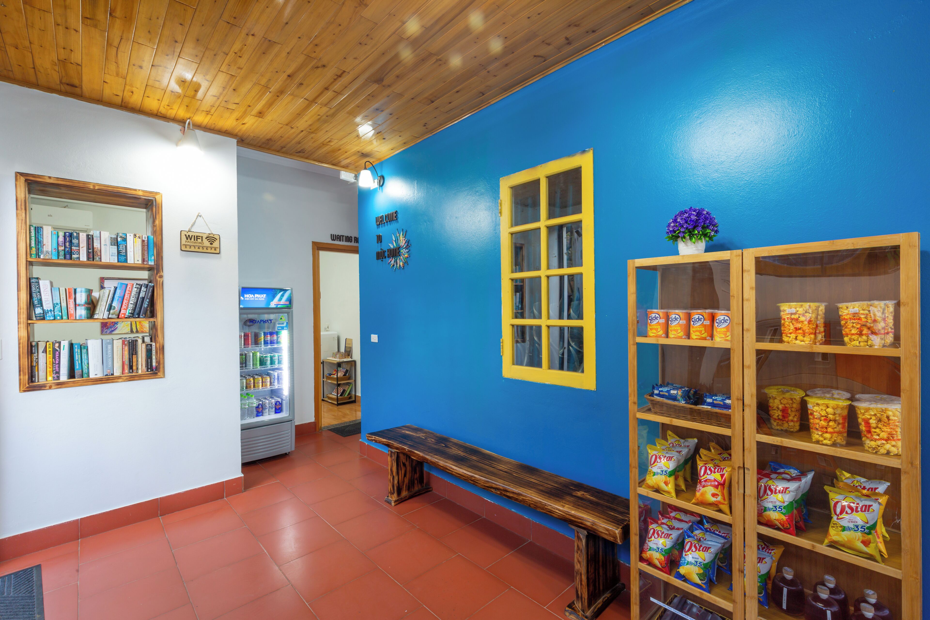 Una habitació amb una banca de fusta, una estanteria, un prestatge per a aperitius i una finestra amb detalls grocs.