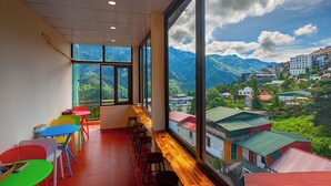 A room with large windows offering a mountain view, colorful chairs, and a wooden table. - Moc Home Sapa Center (Sa Pa)