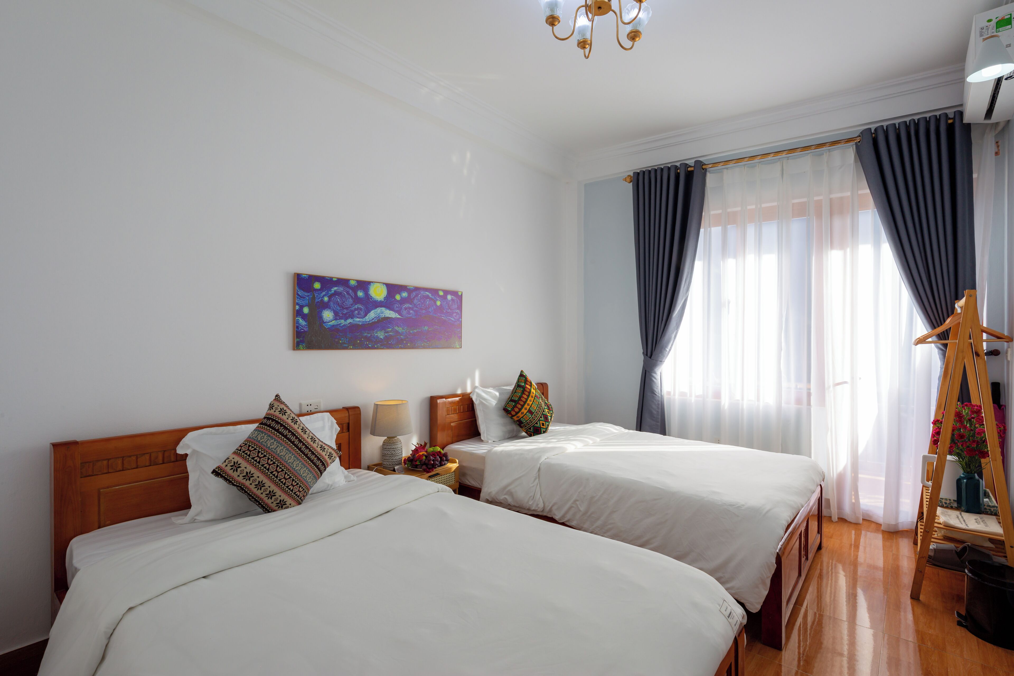 Une chambre d’hôtel avec deux lits, un tableau au mur, un plancher en bois et une fenêtre avec des rideaux.