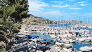 A marina with numerous boats docked, a road with parked cars, and a hilly landscape in the background. - il Rifugio by Interhome (Bordighera)
