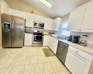 A modern kitchen with white cabinets, stainless steel appliances including a refrigerator, microwave, oven, and dishwasher, and a window providing natural light.