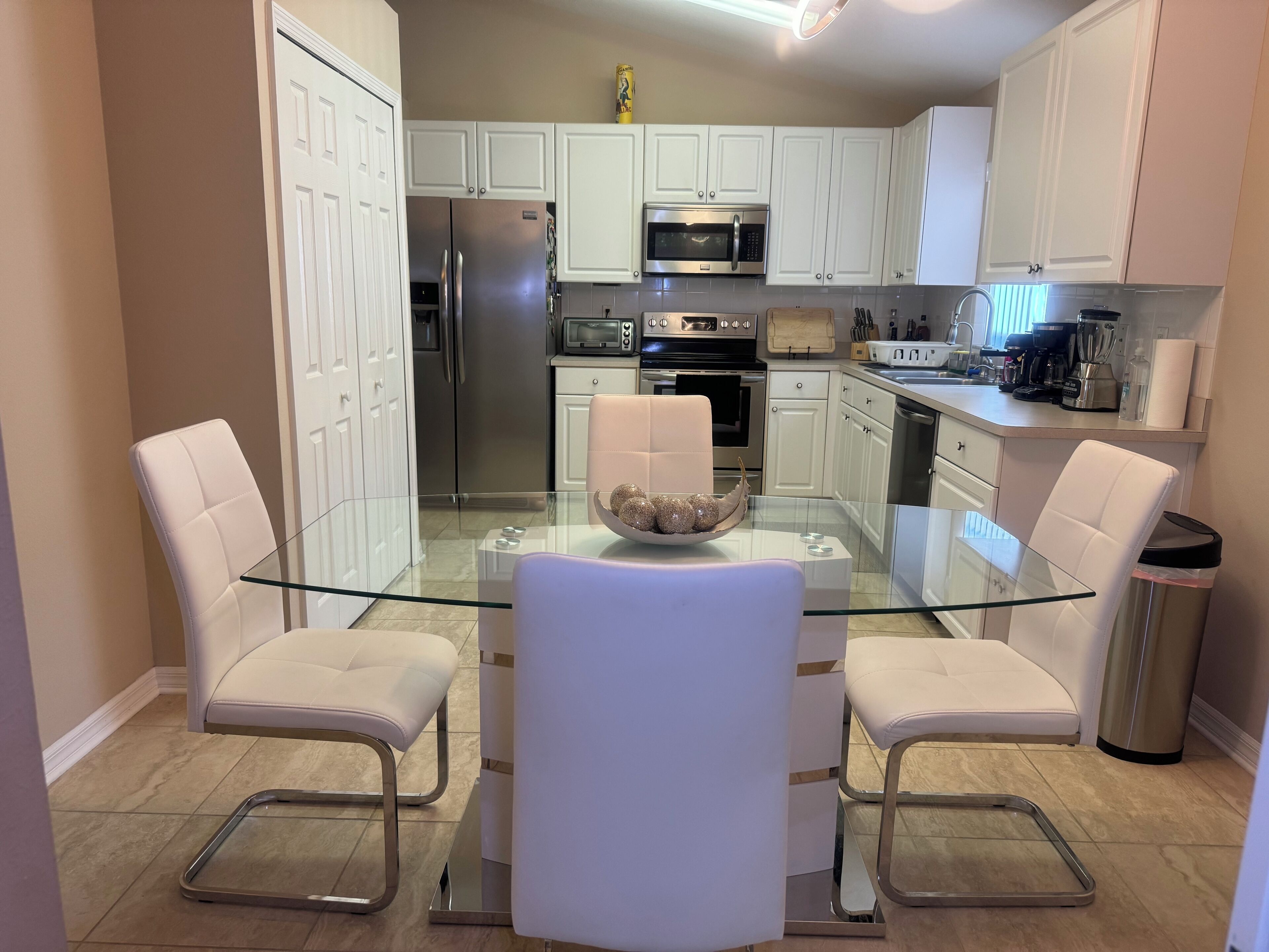 A modern kitchen with white cabinets, stainless steel appliances, a glass dining table, and two white chairs.