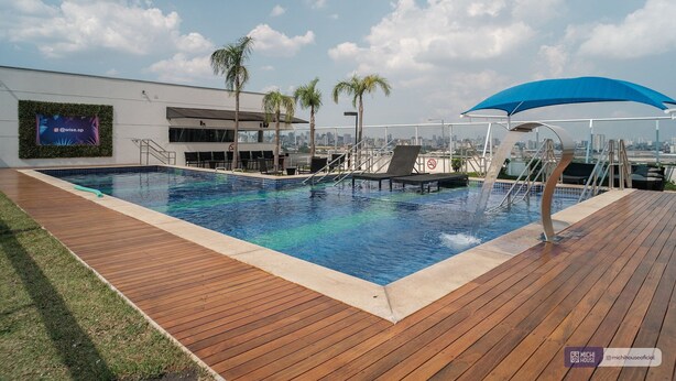 Une piscine avec une terrasse en bois, des palmiers et un auvent bleu.