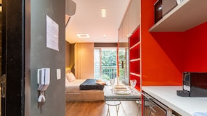 Une chambre d’hôtel compacte comprenant un lit, un coin repas avec une table dressée pour deux personnes, et un mur d’accent de couleur rouge.