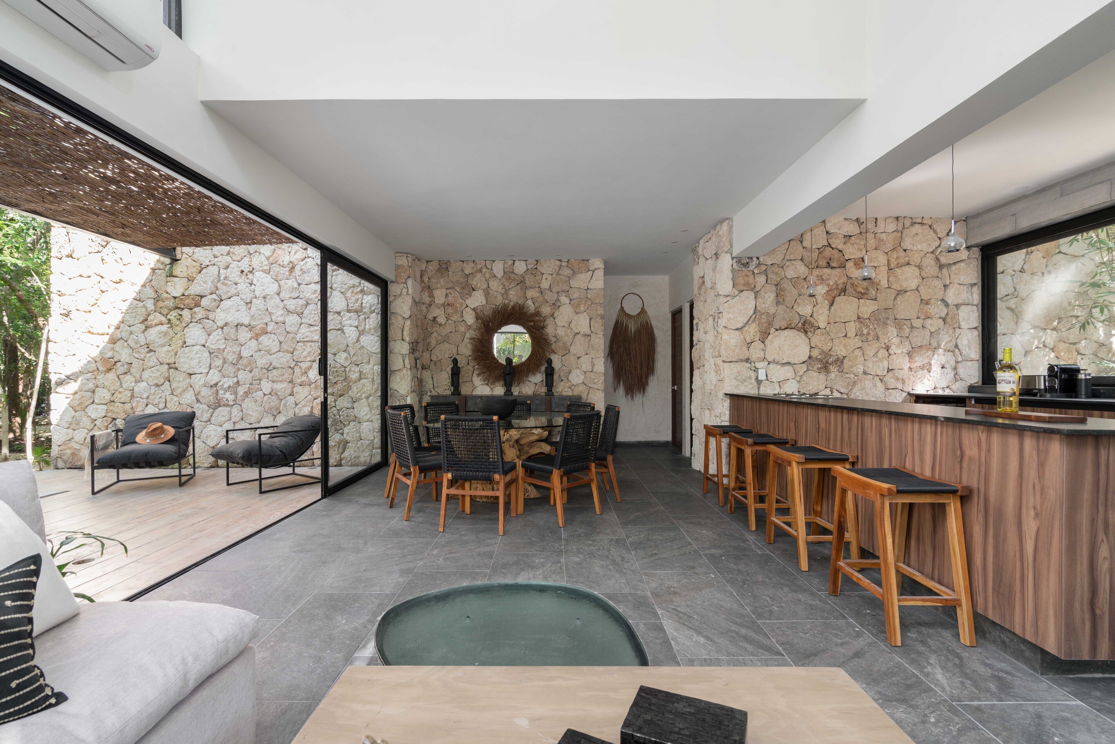 A modern kitchen with a stone wall, wooden bar stools, and a dining area with a round table and chairs.