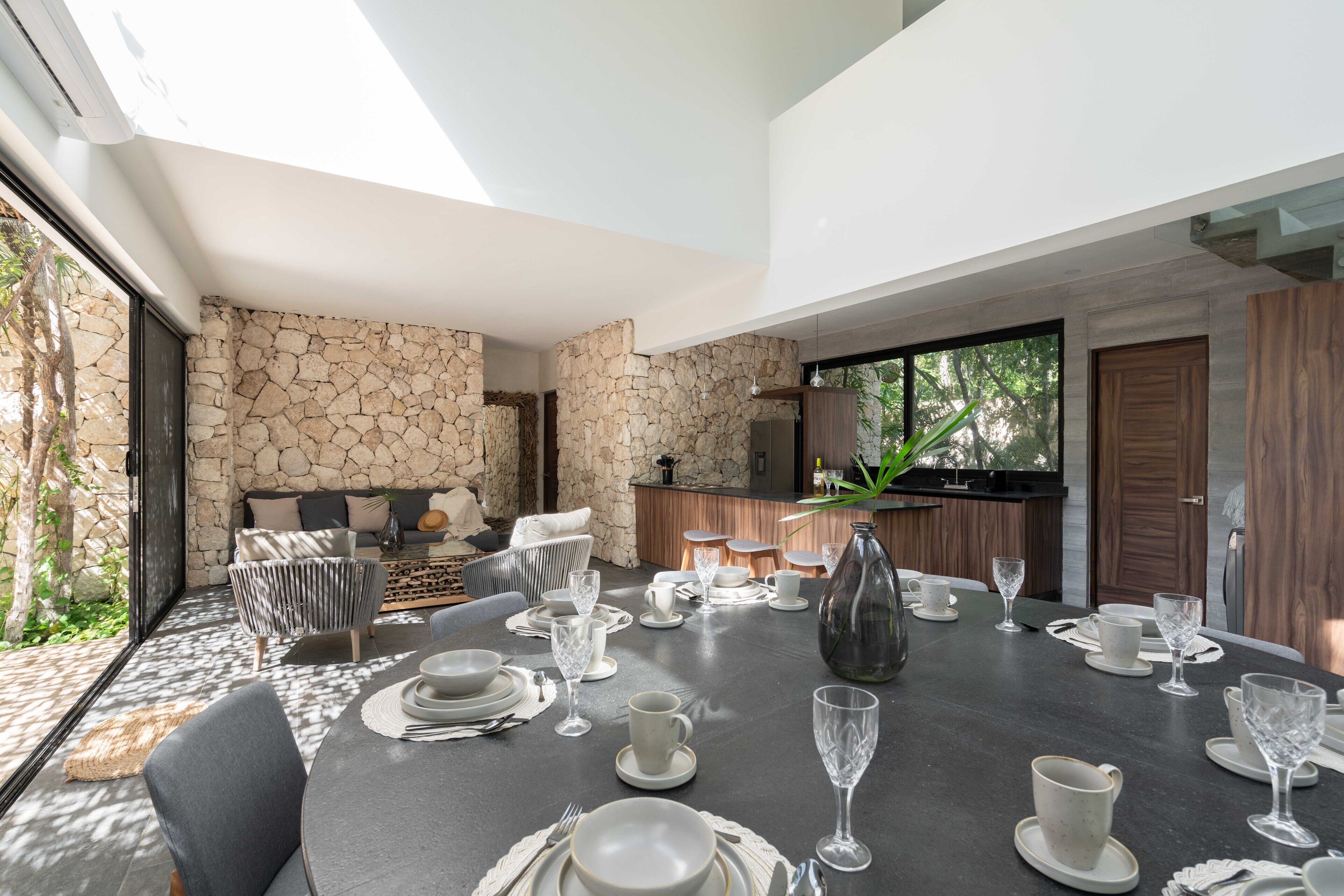 Un área de comedor moderna con una pared de piedra, un sofá y una cocina al fondo.