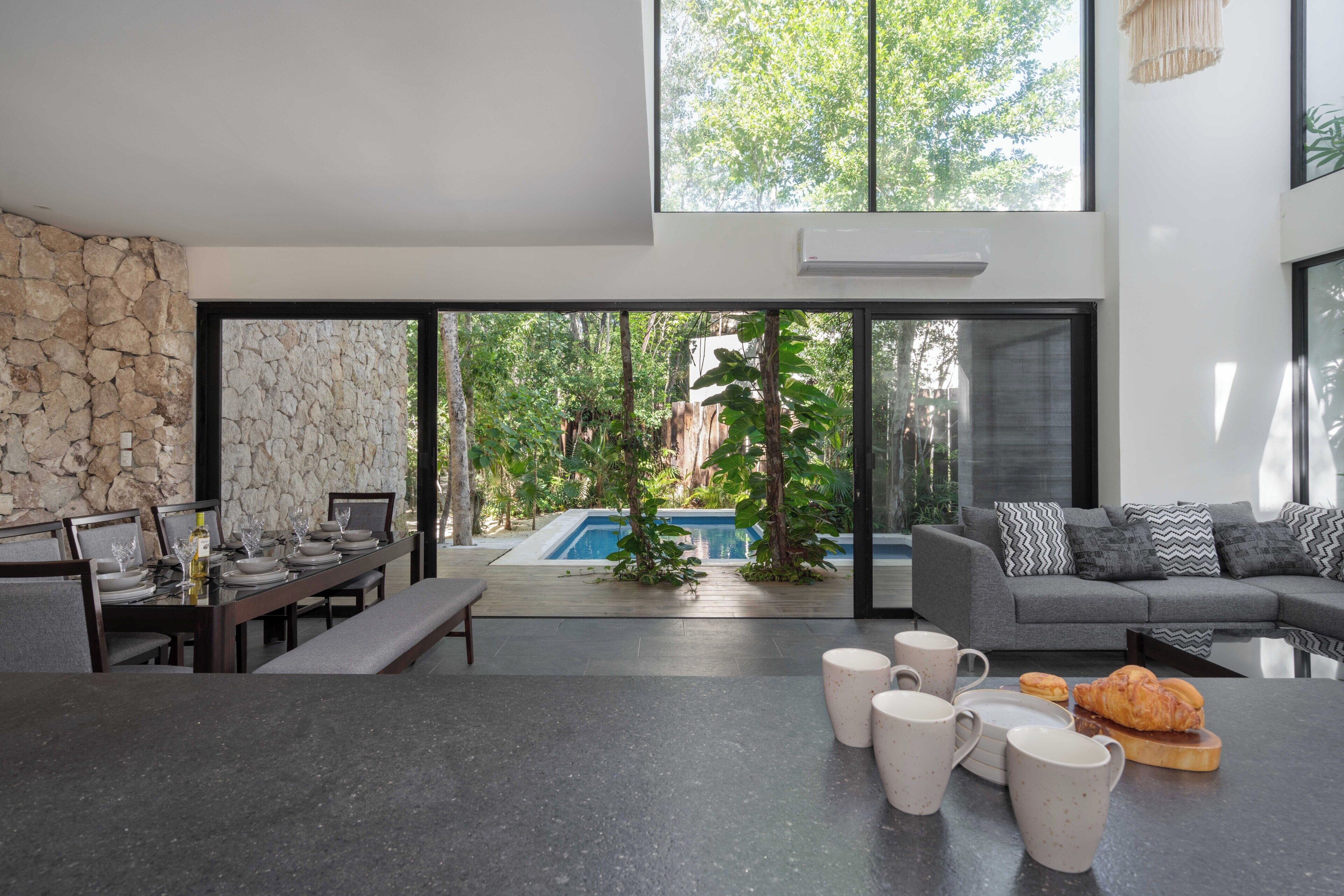A modern living area with a dining table set, a sofa, and a view of a swimming pool.