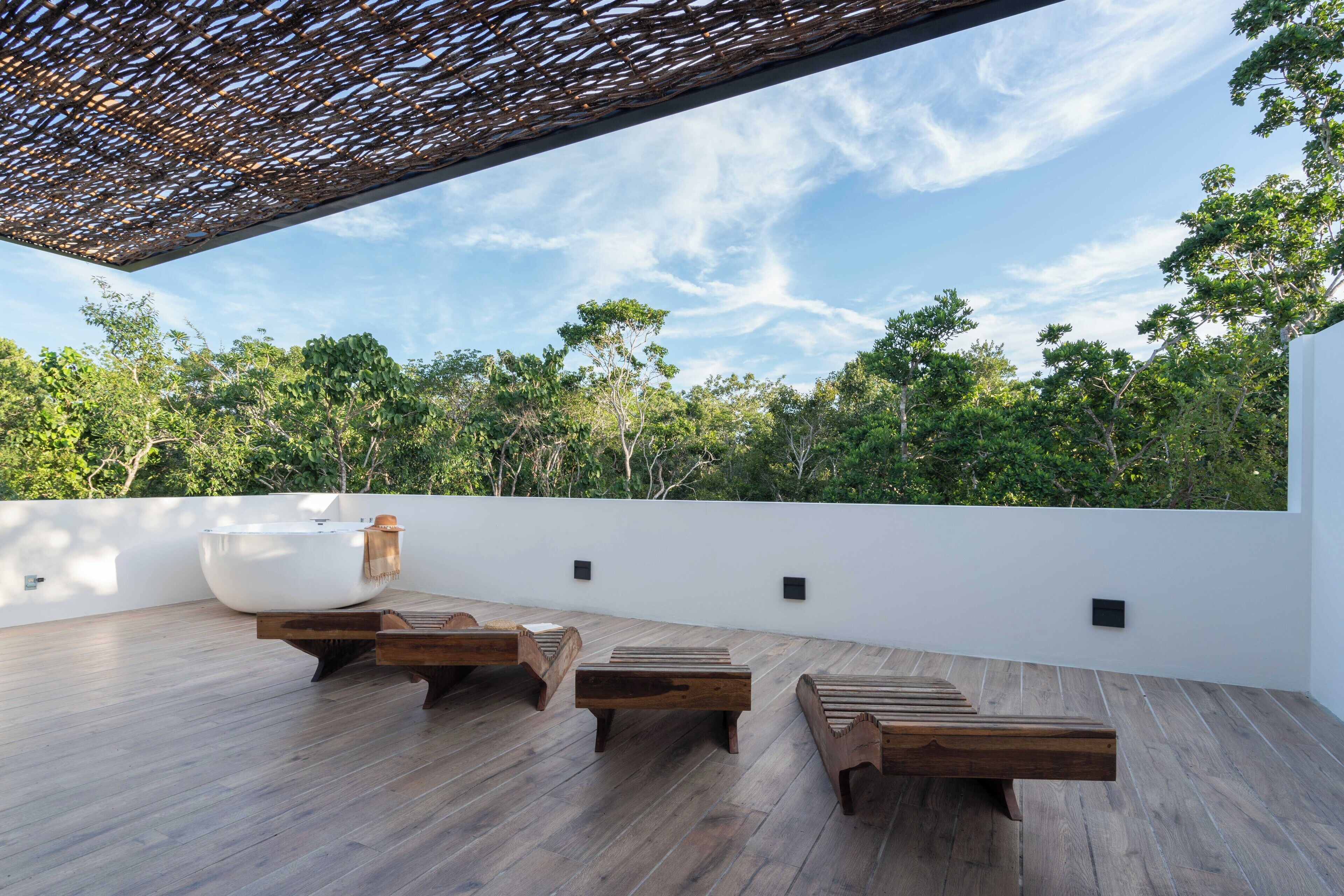 Una terraza en la azotea con tumbonas de madera, un área de descanso con forma de cuenco blanco y vistas a un paisaje boscoso.