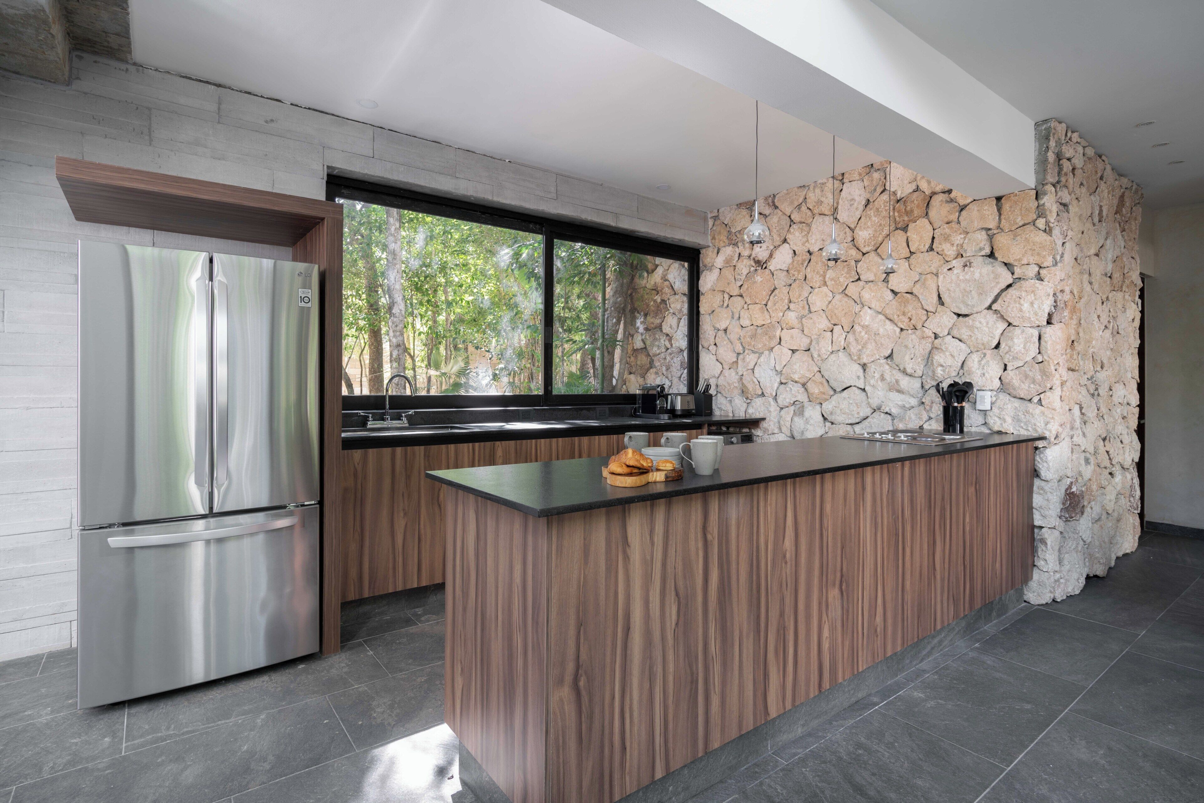 A modern kitchen with a stone wall, a large window, and a built-in island.