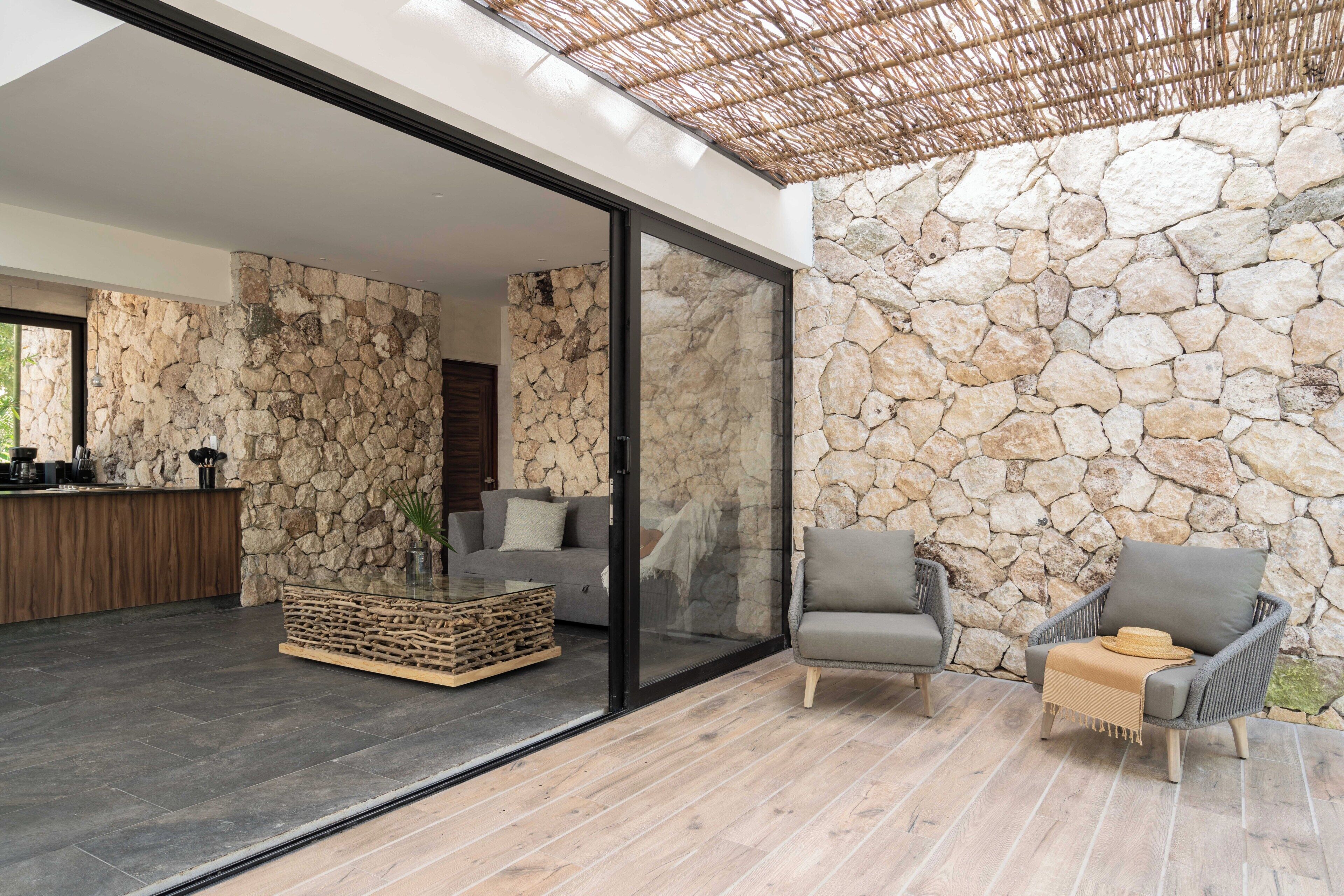 Un interno moderno con pareti in pietra, una porta vetrata che conduce a un balcone e un tavolino da caffè in legno.