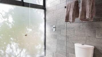 A modern bathroom with a large window, a glass shower enclosure, and a toilet against a tiled wall.