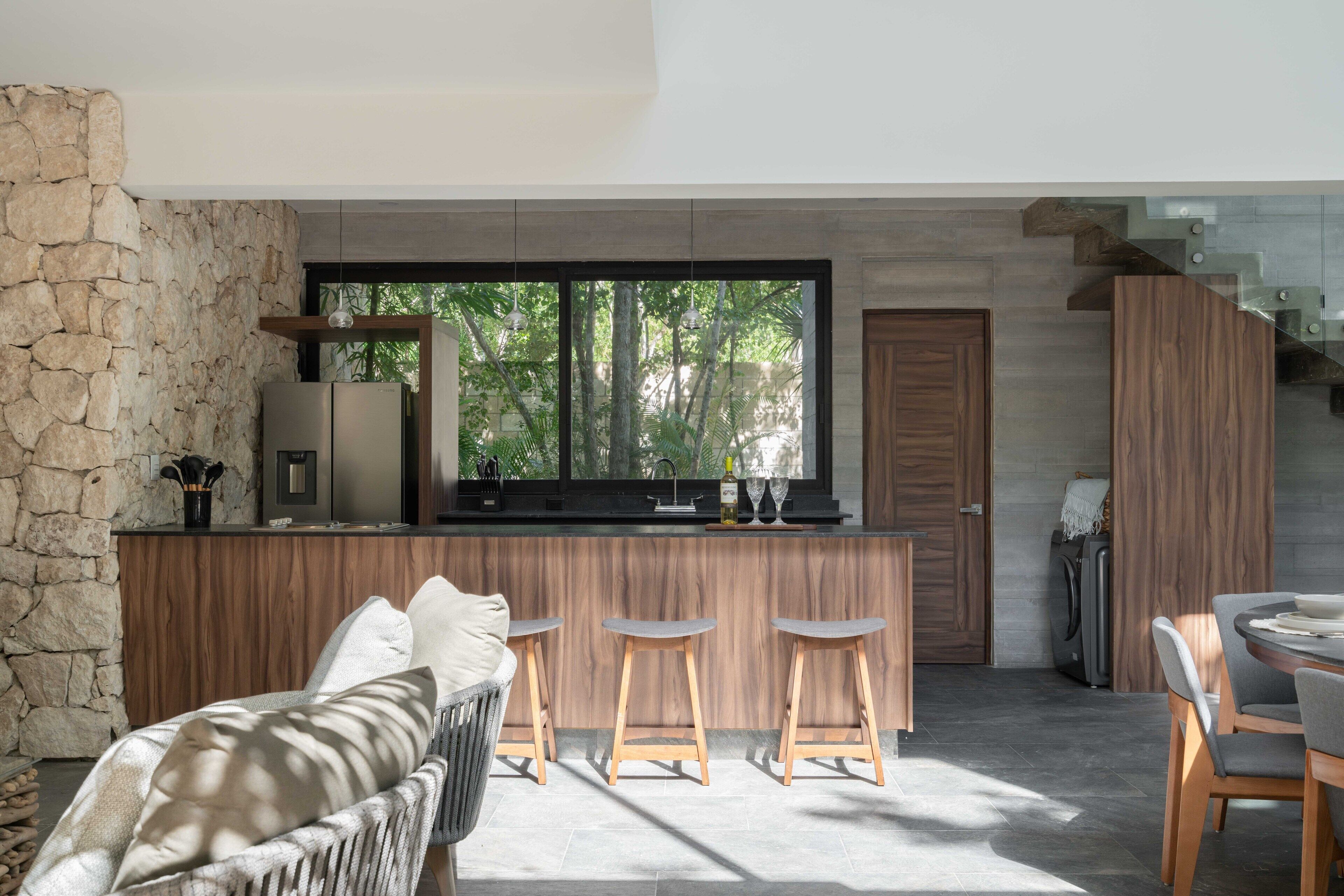 Una cocina moderna con un muro de acento de piedra, un ventanal y un comedor con taburetes de bar.